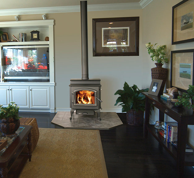 4300 Millennium step top wood stove by Quadra-Fire against a tan wall of a living room with hearth pad