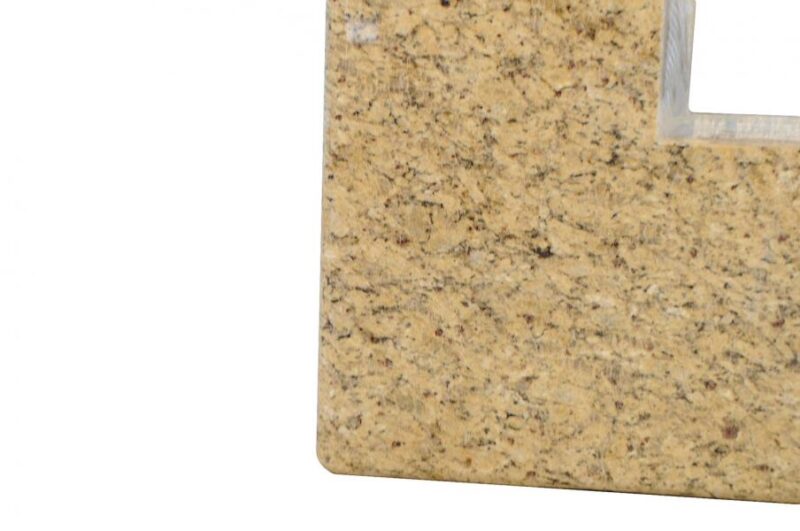 Close-up view of a textured beige granite surface with speckles, focusing on the corner of a square cut-out for a stove.