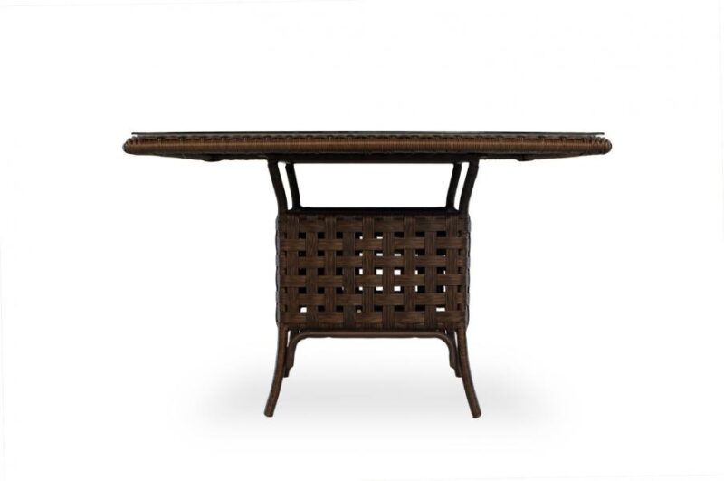 A front view of an oval-shaped rattan coffee table with a woven top and intricate lattice pattern on its sides, standing on four legs, beside a fireplace, isolated on a white background.