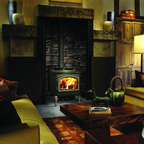 5700 Millennium step top wood stove by Quadra-Fire against a gray stone masonry wall in a living room