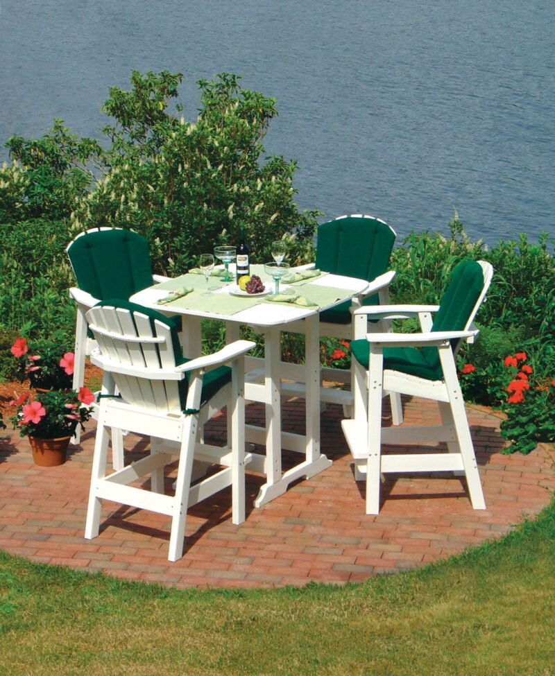 Two green and white adirondack chairs and a small table set up on a lush lawn beside a serene lake, with a wine bottle and glasses on the table, surrounded by blooming flowers and
