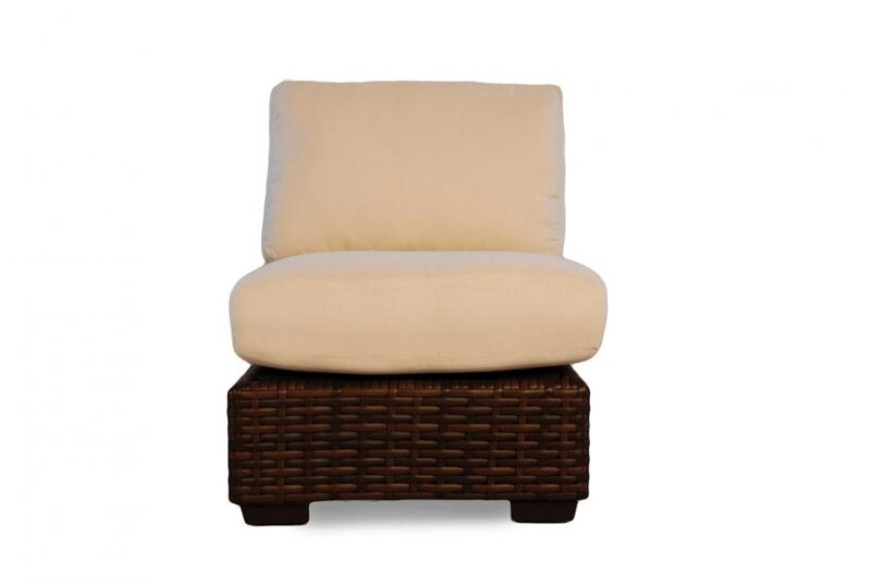 A light beige cushioned armless chair with a dark brown woven wicker base, set against a plain white background near a fireplace.