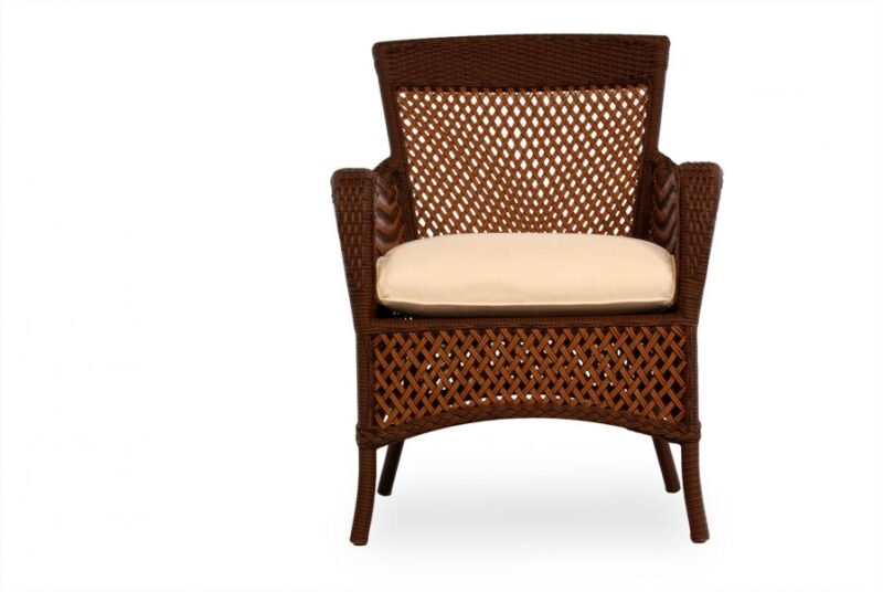 A wicker armchair with a tall back and mesh-like pattern, featuring a light beige cushion on the seat, isolated on a white background beside an elegant fireplace.