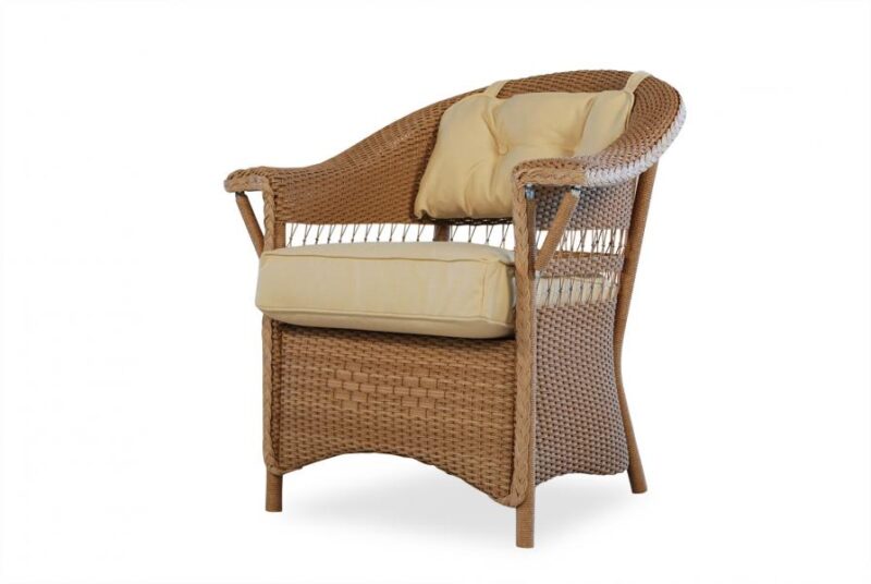 Wicker armchair with beige cushions on a white background, featuring a woven design and built-in magazine holders on the sides, positioned near a fireplace.