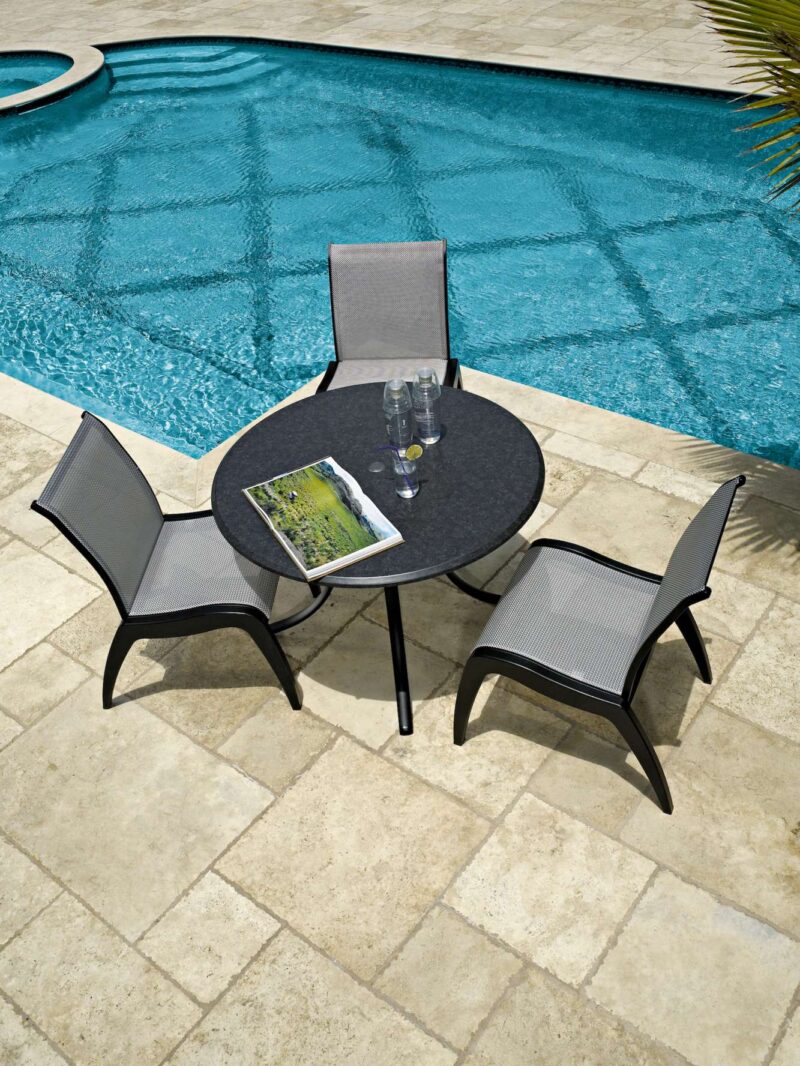 Patio set with a round table and two chairs beside a blue swimming pool, featuring a magazine and glasses on the table with an insert fire pit.