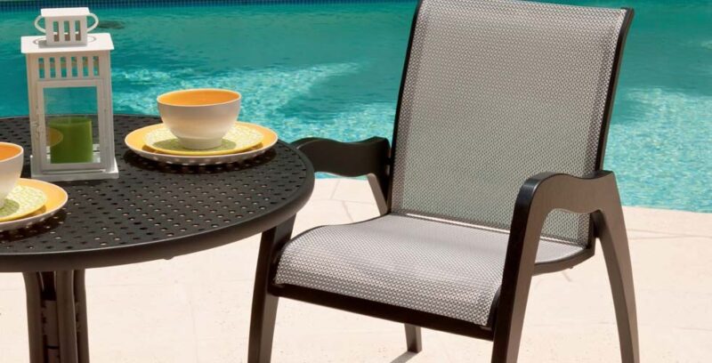 Outdoor patio setting featuring a round black table with two plates and cups, a chair, and a lantern beside a turquoise swimming pool includes an insert fireplace.