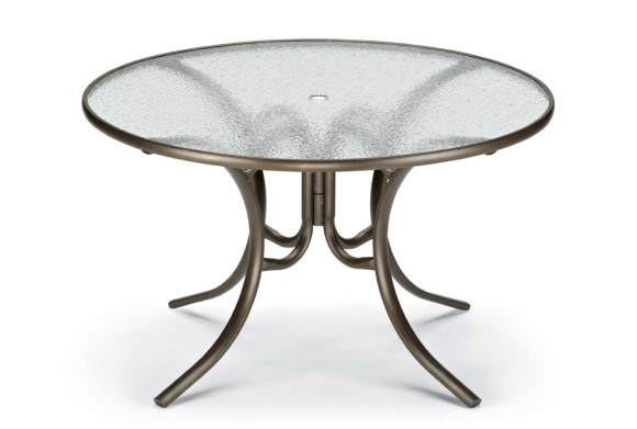 A round glass-top table with a metallic base featuring curved legs, isolated on a white background, ideal for placement near a fire pit.