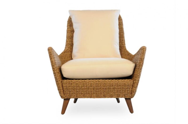 A modern wicker armchair with beige cushions on a white background, featuring angled wooden legs and high armrests near a fireplace.