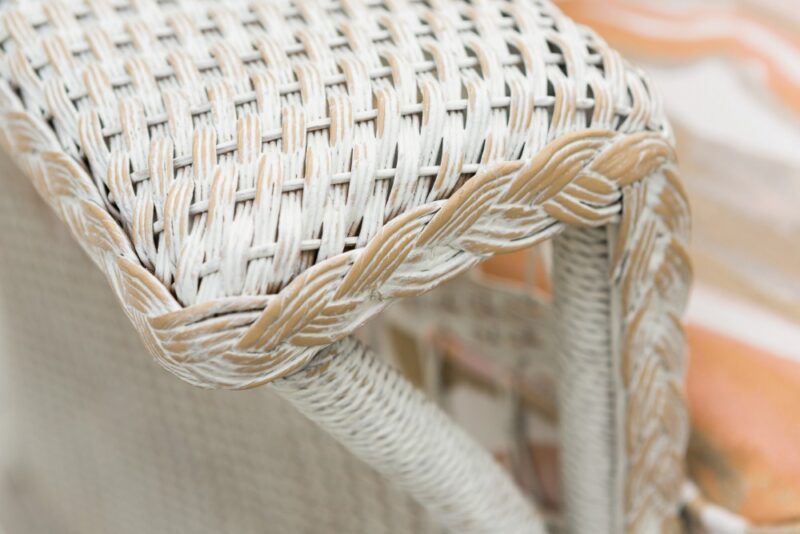 Close-up of a woven wicker chair arm demonstrating intricate weaving details and textures, with soft, blurred background colors near a fireplace.