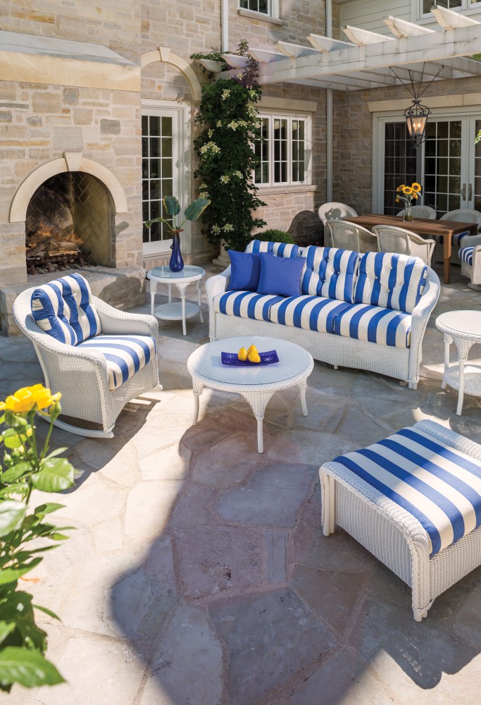Outdoor patio furniture with blue and white striped cushions set on a stone floor, complete with a fire pit, in a cozy, elegant home exterior.