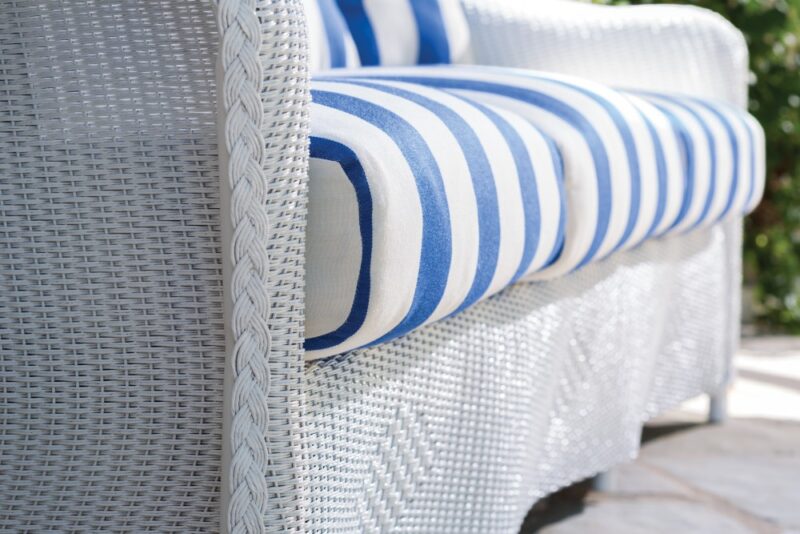 Close-up of a wicker couch with white and blue striped cushions, highlighting the texture of the woven material. The setting appears to be outdoors with natural light near a fireplace insert.