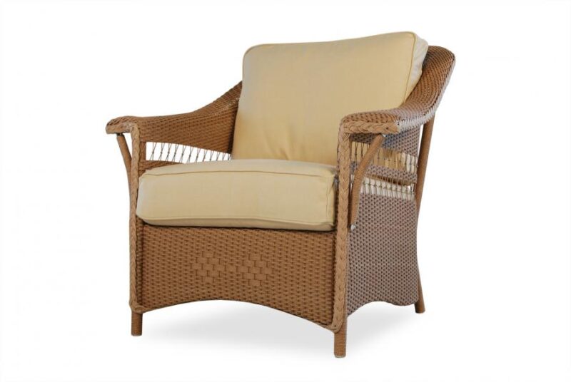 A rattan armchair with beige cushions against a white background. The chair has a high back, weaved side panels near a fireplace, and a cushioned seat and backrest.