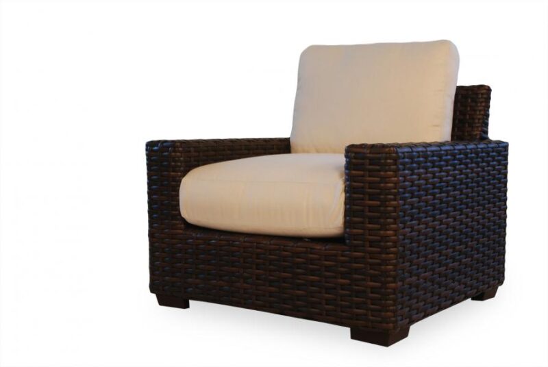 A modern armchair with dark brown woven wicker frame and a plush cream cushion, isolated near a fireplace on a white background.