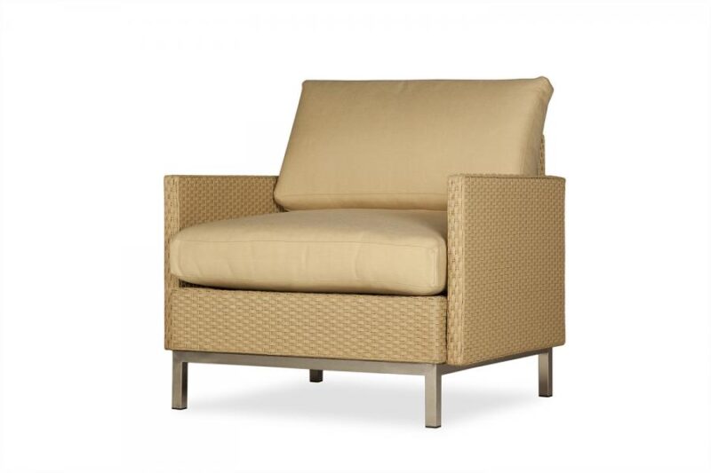 A modern beige armchair with thick cushions and a woven frame, set against a plain white background, near an elegant fireplace.