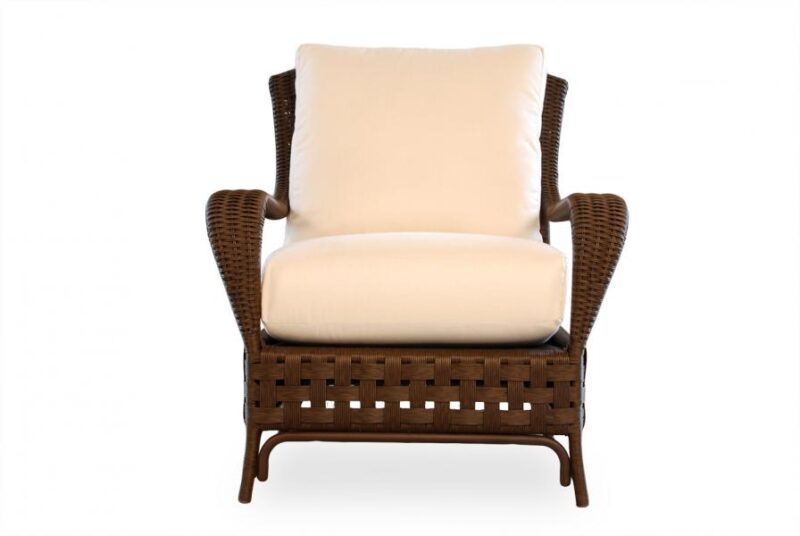 A wicker armchair with a plush, cream-colored cushion on a white background. The chair features a sturdy, woven base and comfortable armrests near a cozy fireplace.