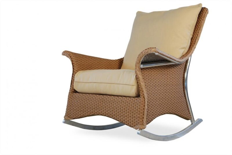 A modern wicker rocking chair with beige cushions beside a fireplace on a white background.