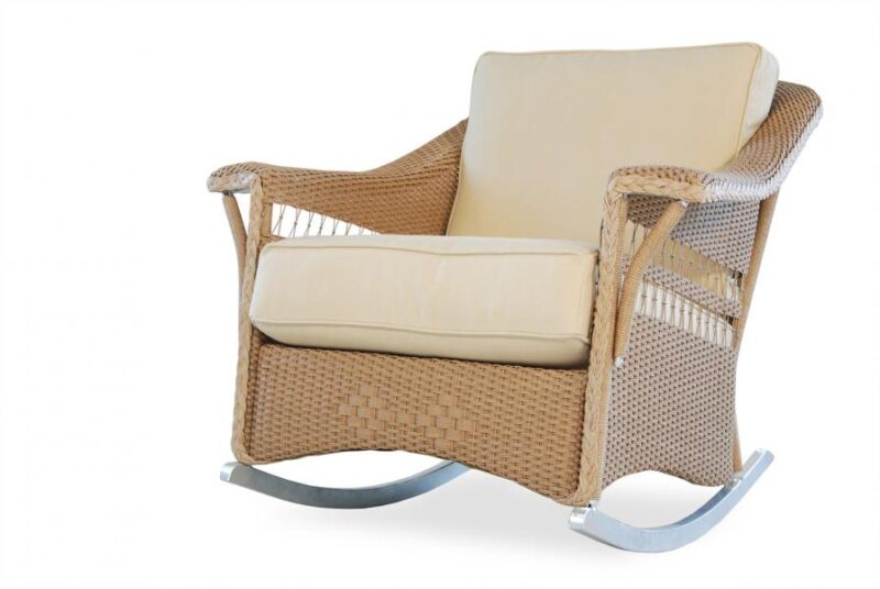 A modern rocking chair with a woven beige frame and plush cream cushions, set against a white background by a cozy fireplace.
