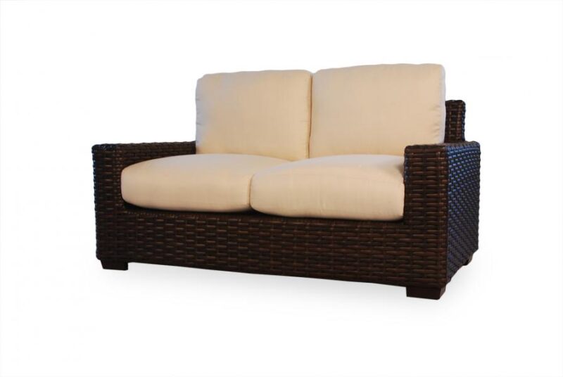A dark brown wicker loveseat with two plush beige cushions near a fireplace against a white background.