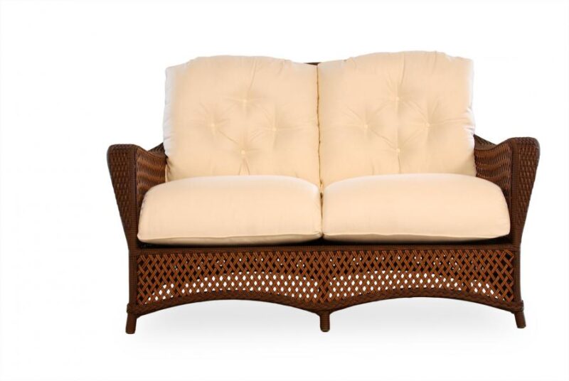 A brown wicker two-seater sofa with plush cream-colored cushions, near a fireplace, isolated on a white background.