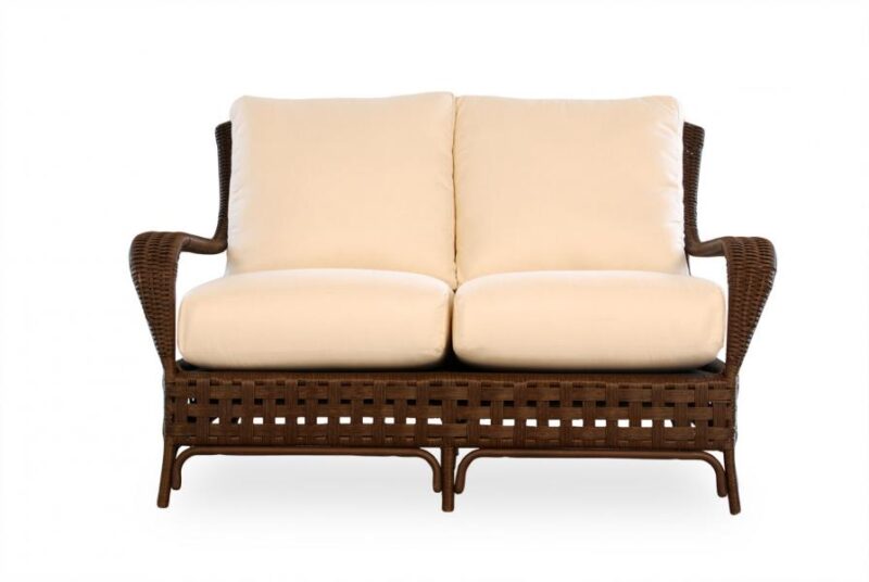 A two-seater rattan sofa with plush cream cushions, isolated on a white background, positioned near a fireplace.