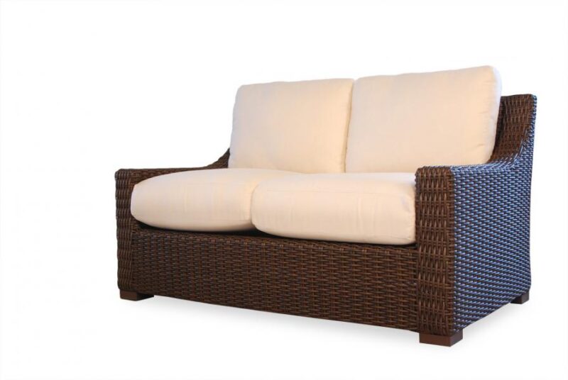 A modern two-seater sofa with a dark brown wicker frame and plush cream cushions, isolated on a white background, features an integrated fire pit.