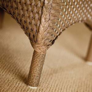Close-up view of a wicker chair leg near a fireplace, showing detailed weaving patterns and natural fiber textures.