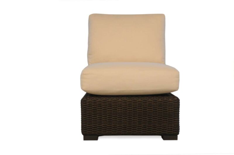 A modern armchair with a beige cushion on a dark brown wicker base, set near a cozy fireplace, against a plain white background.