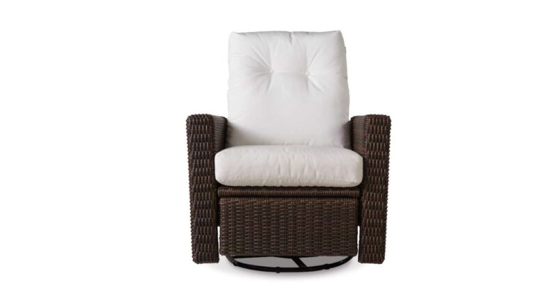 A modern swivel rocker chair with a dark brown wicker frame and plush white cushions, isolated near a fireplace on a white background.