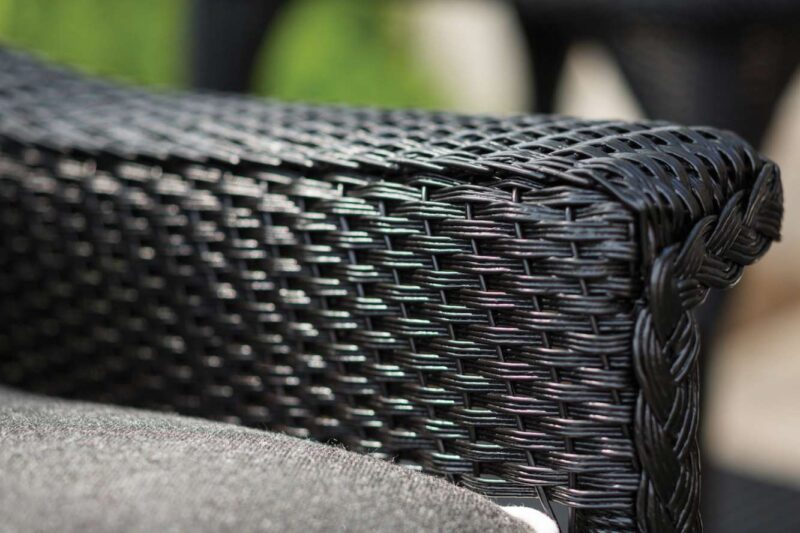 Close-up of the woven texture of a black wicker chair arm by the fireplace, with blurred background emphasizing the detail and craftsmanship of the weave.