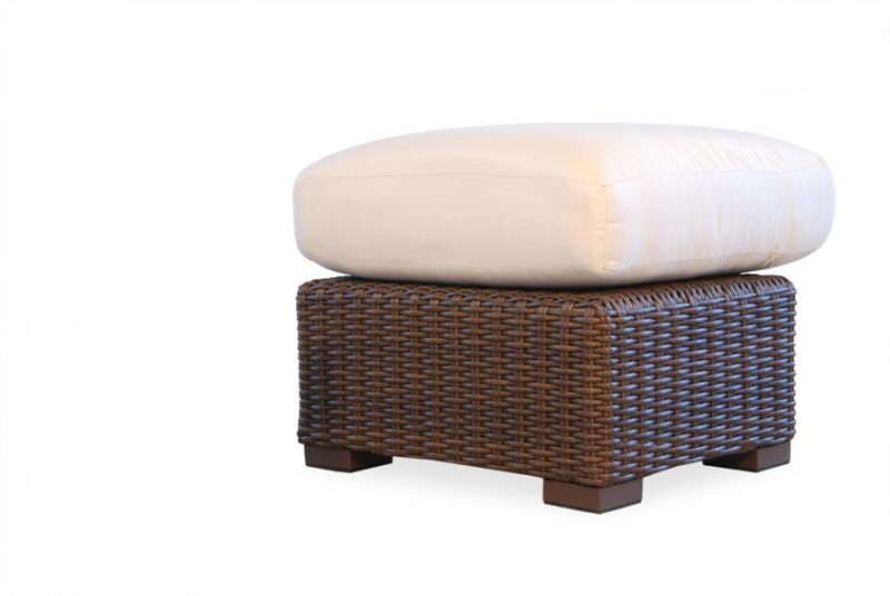 A large, plush white cushion resting on top of a dark brown wicker ottoman with wooden legs, isolated on a white background near a fireplace insert.