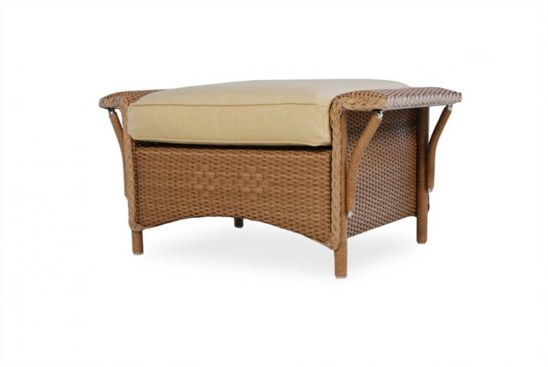 A wicker outdoor ottoman with a tan cushion on top and a lower shelf, isolated on a white background.
