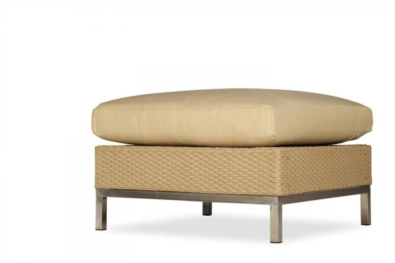 A light beige cushion resting on a beige woven ottoman with a sleek metal frame, isolated against a white background with a fireplace insert.