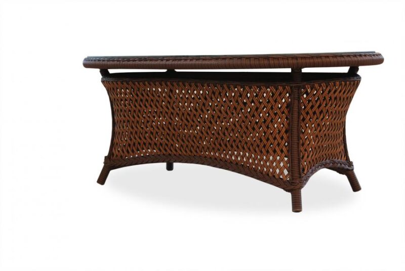 Wicker coffee table with a curved design and glass top, set against a white background near a fireplace. The table features intricately woven patterns and sturdy legs.