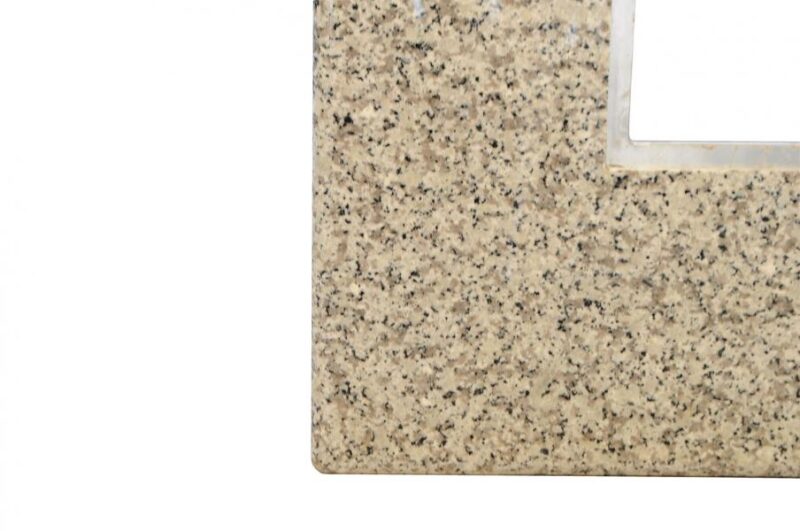 Close-up of a beige granite surface with speckled pattern and a cut-out square on the left side, showing detailed texture and edges around a stove.