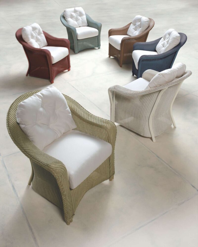 Five elegant wicker armchairs with cushioned seats, in varying colors of red, tan, blue, white, and green, arranged around a fire pit on a neutral tiled floor.