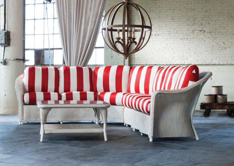 A stylish living room with a red and white striped sofa and a matching wicker chair, set against a rustic brick wall with a large spherical wooden frame decor hanging above, featuring an elegant stove insert.