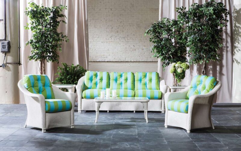 Elegant indoor lounge area featuring a green and white striped sofa set with matching armchairs, adorned with plants, against a brick wall backdrop that incorporates a stylish fireplace insert.