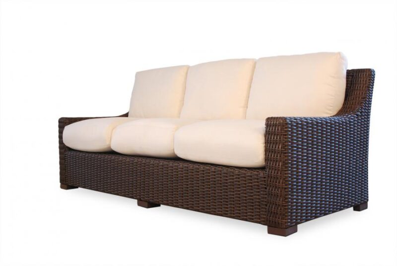 A wicker sofa with a dark brown base and three plush beige cushions, isolated on a white background near a fire pit.