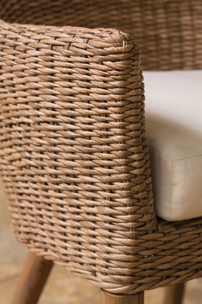 Close-up of a wicker chair showcasing its intricate weave pattern and wooden frame, with a beige cushion partially visible near a fireplace.