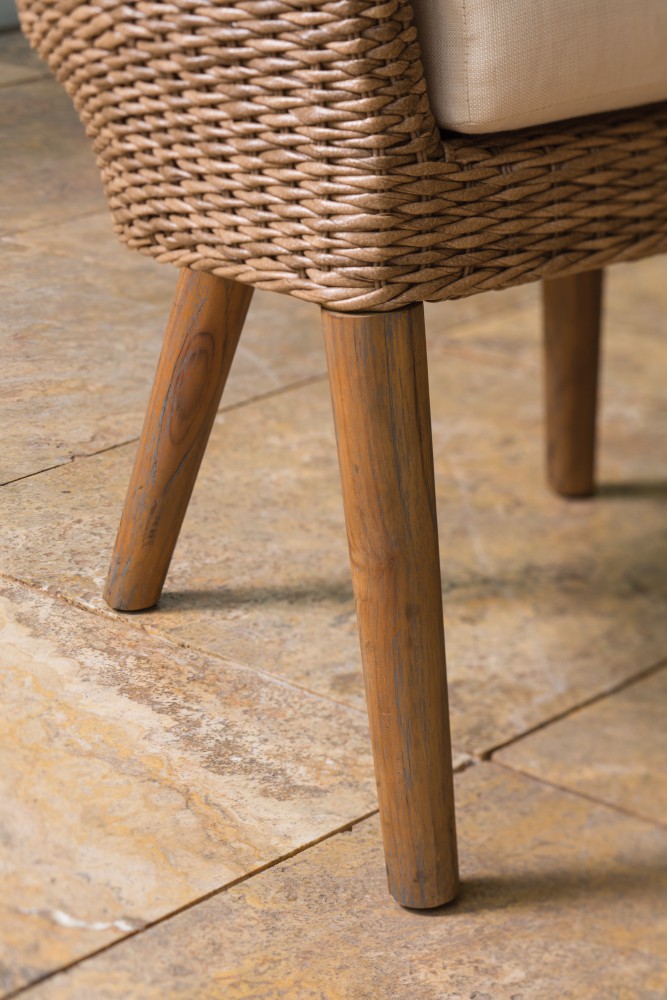 Close-up of a chair with wicker detailing and wooden legs near a fireplace on a textured stone floor.