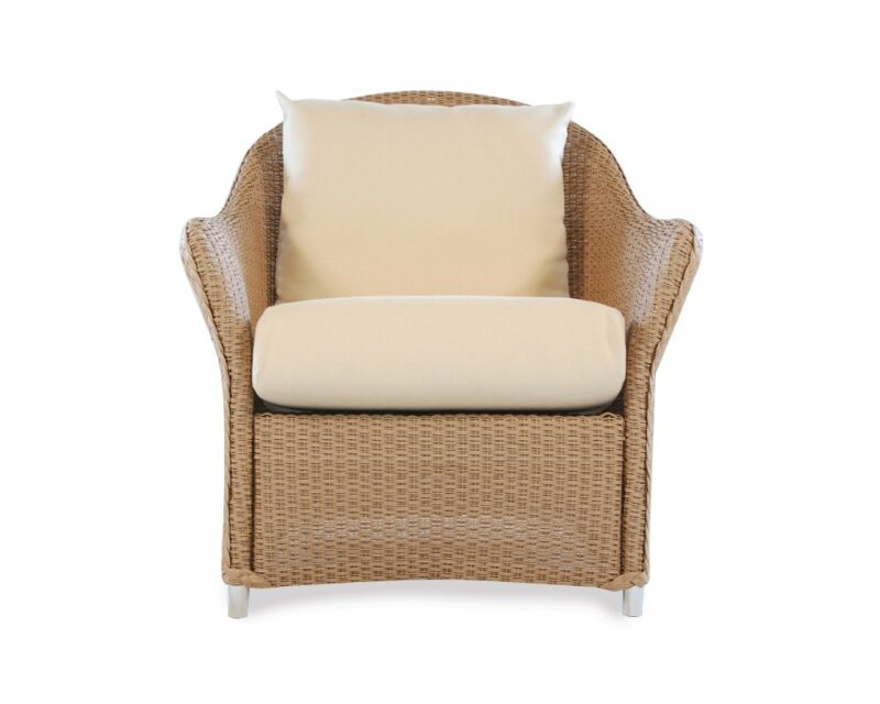A front view of a wicker armchair with a beige cushion and a small pillow against a white background, near a cozy fireplace.