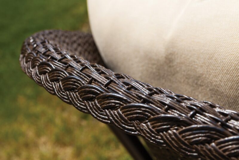 Close-up view of a woven wicker armrest of a patio chair with a beige cushion, situated beside a fire pit, showcasing the texture and intricate weaving pattern.