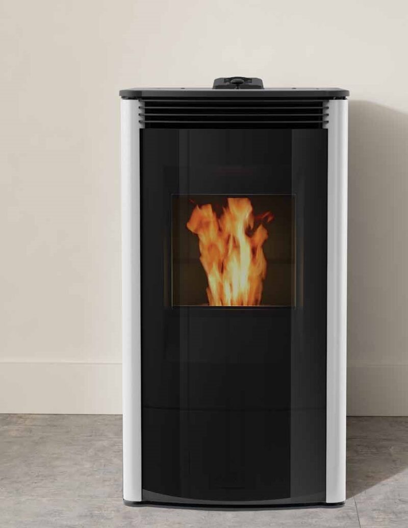 A modern pellet stove with a visible fire burning inside, set against a plain beige wall and grey floor. The stove is mostly black with a white top and base.