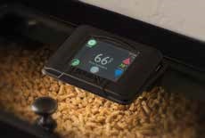A digital device displaying a temperature of 66 degrees sits on top of a stove filled with wood pellets, suggesting the monitoring of stove temperature.