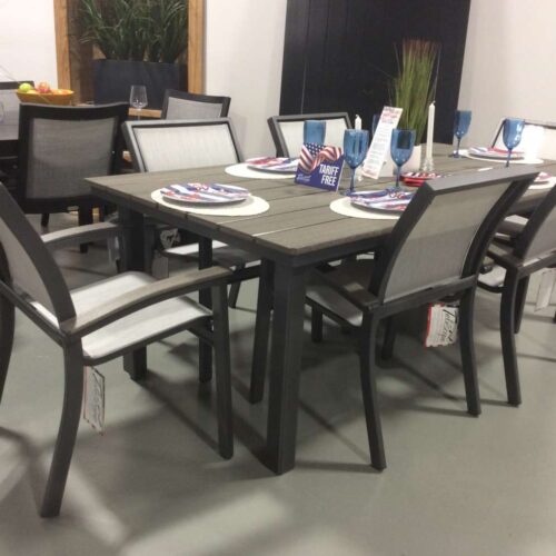 A dining table set with six chairs in a showroom, featuring placemats, patriotic decor, and a stove on a side counter.