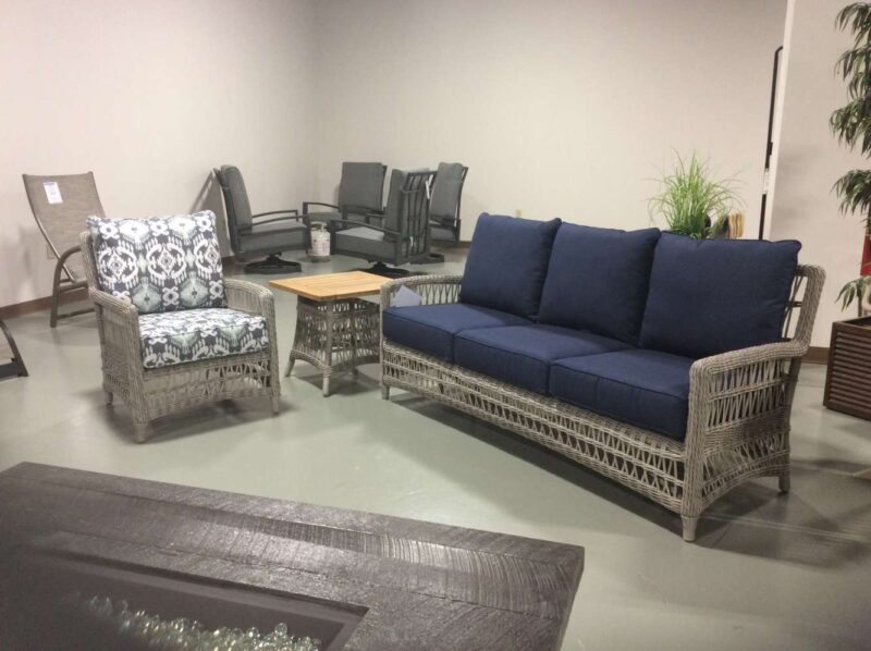 Modern office lounge featuring a dark blue sofa, patterned armchair, and mesh-back office chairs around wooden tables, with a fireplace adding warmth along with plants that introduce a touch of greenery.