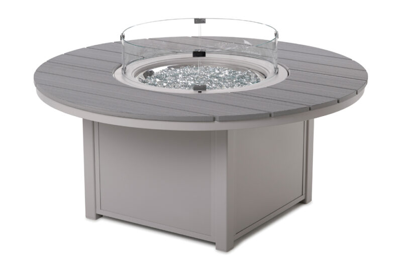 A modern grey circular fire pit insert with a glass wind guard and visible reflective glass rocks, set on a white background.