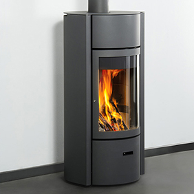 A modern, black wood-burning stove insert with visible flames behind a glass door, installed in a corner against a grey wall.