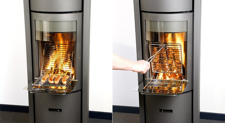 A vertical rotisserie stove with glass doors. The left side shows sausages cooking inside, and the right side displays a hand using tongs to remove one sausage from the top tray.
