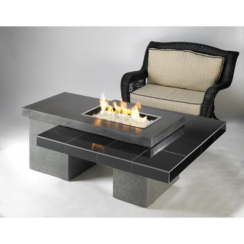 A modern outdoor furniture setup featuring a square fire pit table with a visible flame, surrounded by a sleek, gray base, next to a rattan armchair with beige cushions.